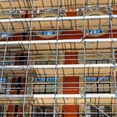 Scaffolding covers the facade of a red-brick building with large windows and decorative stonework, indicating construction or restoration work in progress.