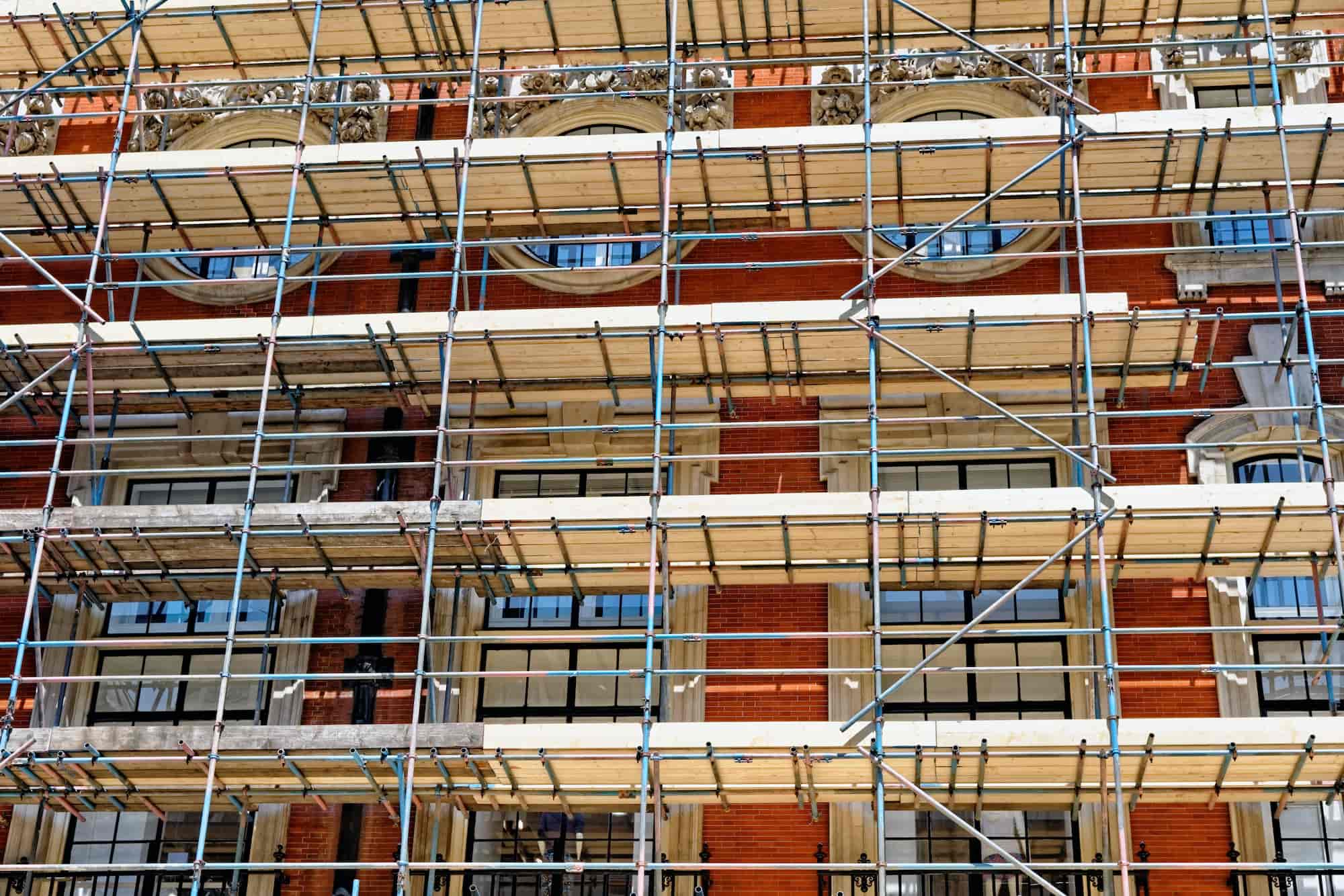 Scaffolding covers the facade of a red-brick building with large windows and decorative stonework, indicating construction or restoration work in progress.